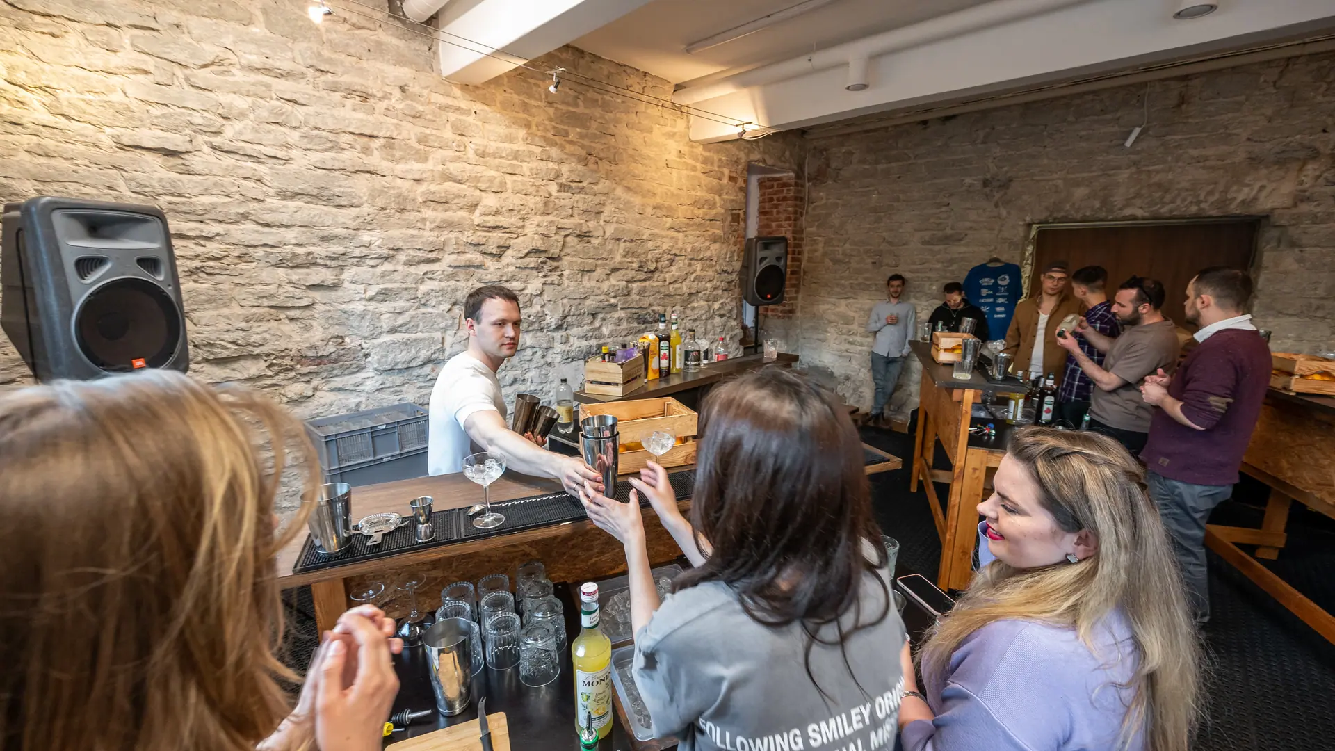 Cocktail workshop: the bartender guiding the group across the counter in a stone-walled hall