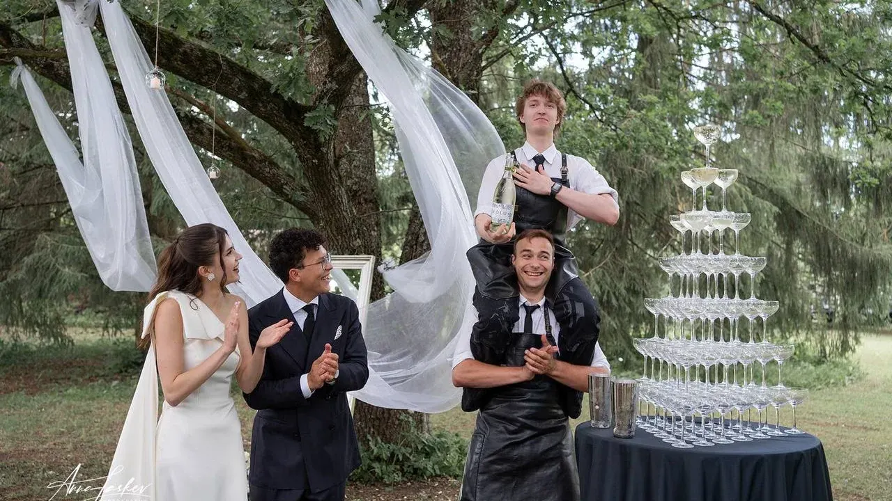 The couple watching the bartender fill the glass pyramid under the oak