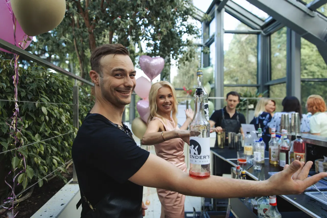 A bartender presenting a Bartender’s bottle behind the counter, guests and balloons in the background