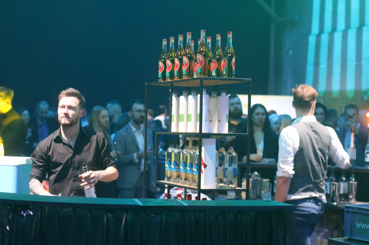 Mobile bar at a corporate event: a bottle display in blue stage light, bartenders and the crowd