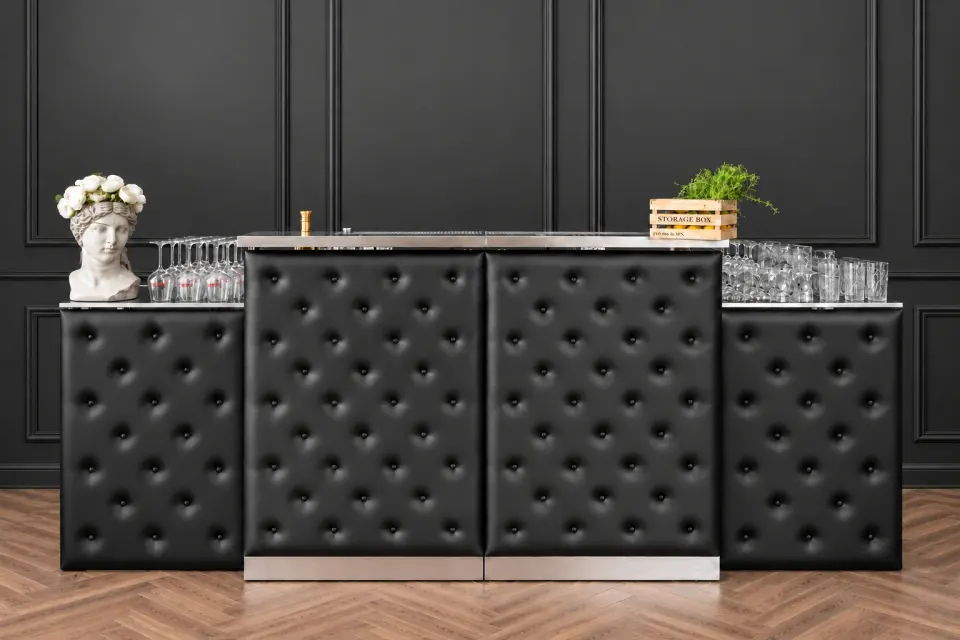 Black tufted modular bar counter in a dark interior, with glassware and flowers on top